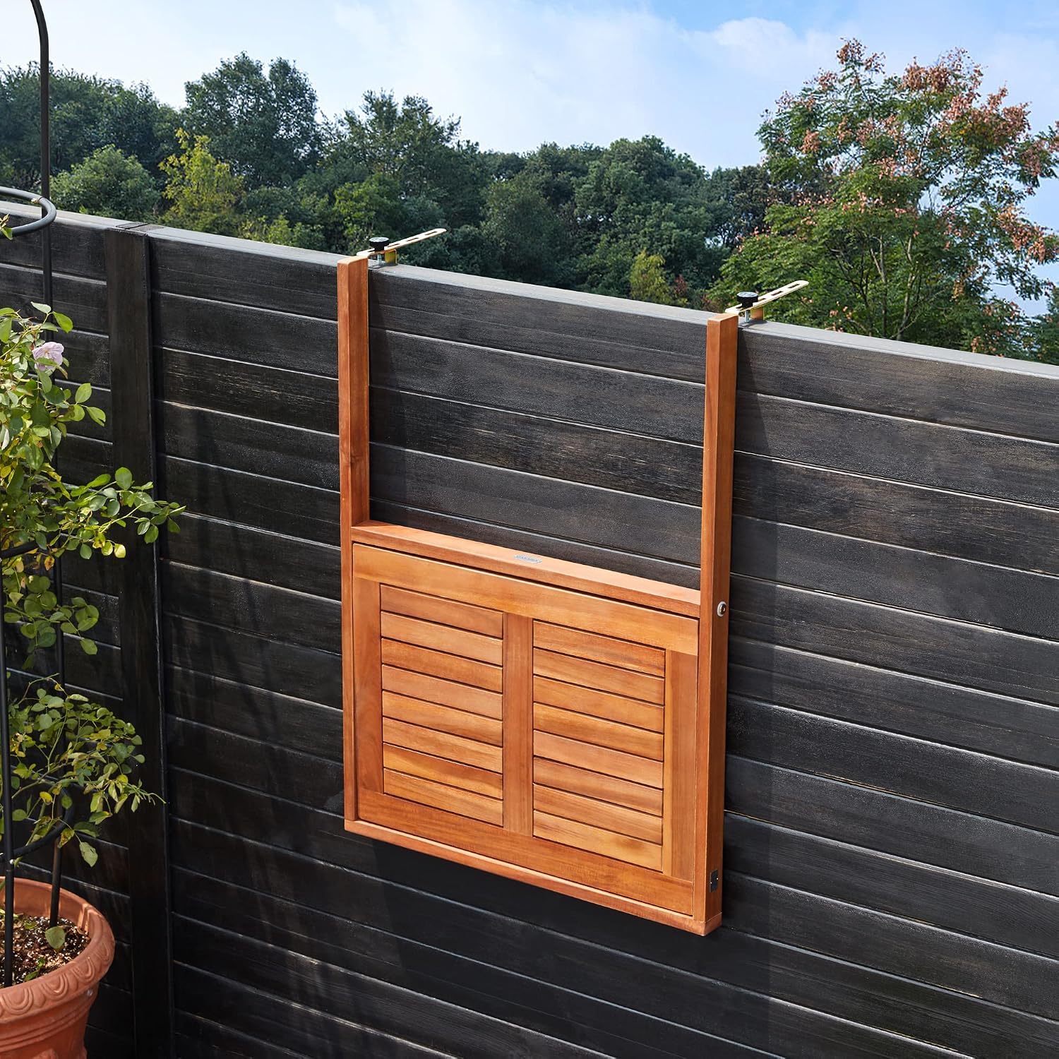 Casaria balcony table in its folded position, flat against a black wooden fence.