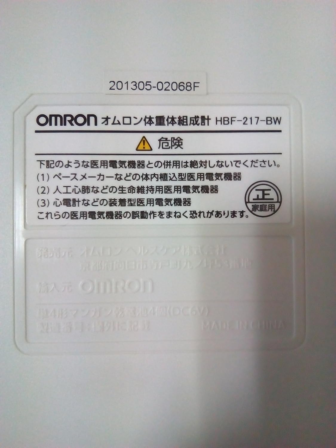 Close-up of the product label on the bottom of the OMRON HBF-217-BW Body Composition Monitor, showing model number and safety warnings.