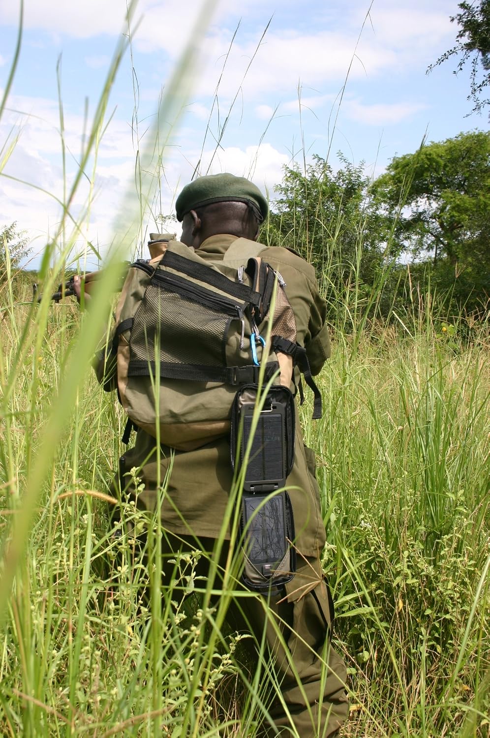 Person with a backpack, with the Powertraveller Solarmonkey Adventurer attached, walking through tall grass.