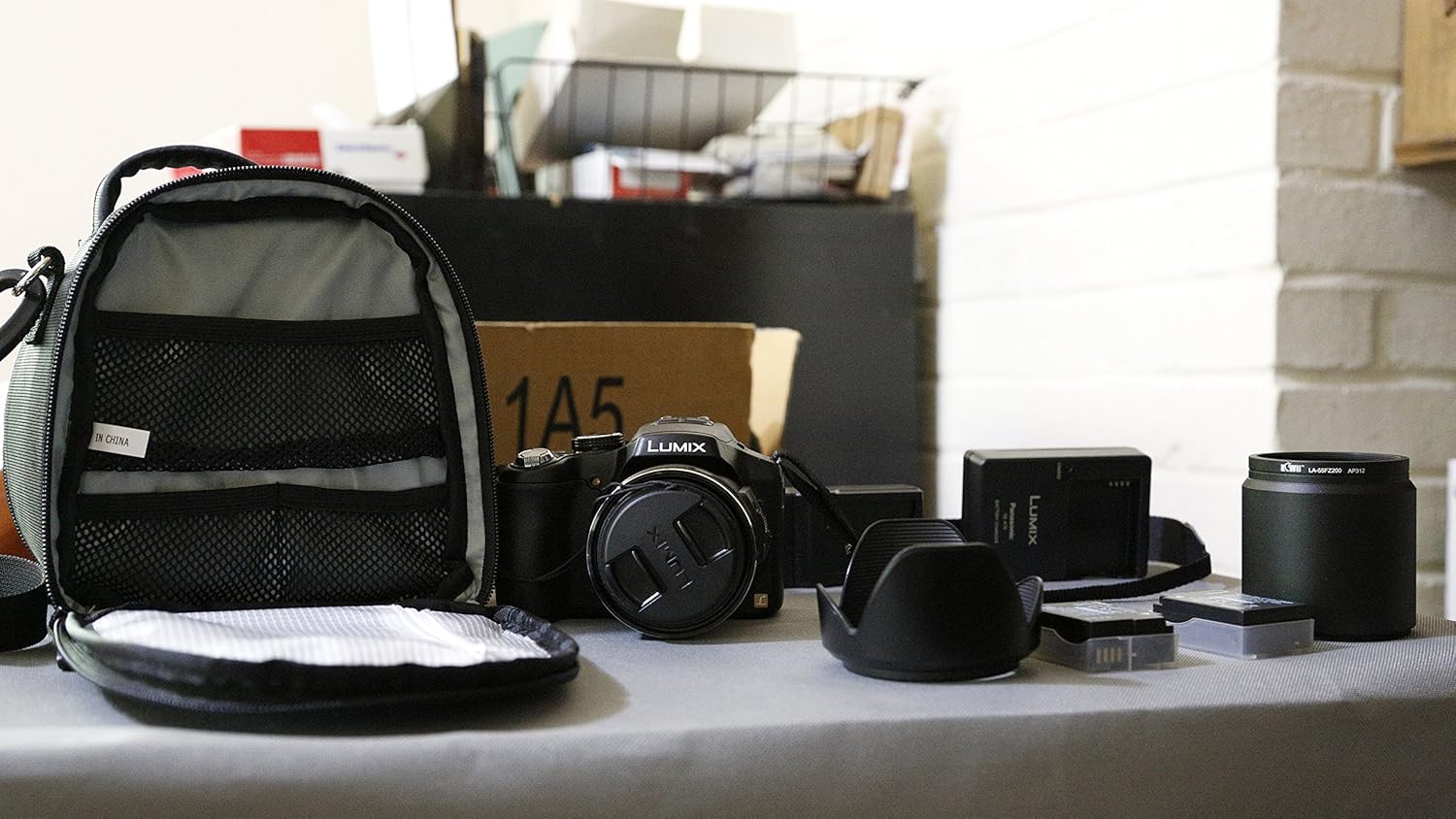 Panasonic Lumix DMC-FZ200 kamera kitinin içeriği, kamera, çanta, şarj cihazı ve diğer aksesuarlar dahil olmak üzere bir masanın üzerinde sergileniyor.