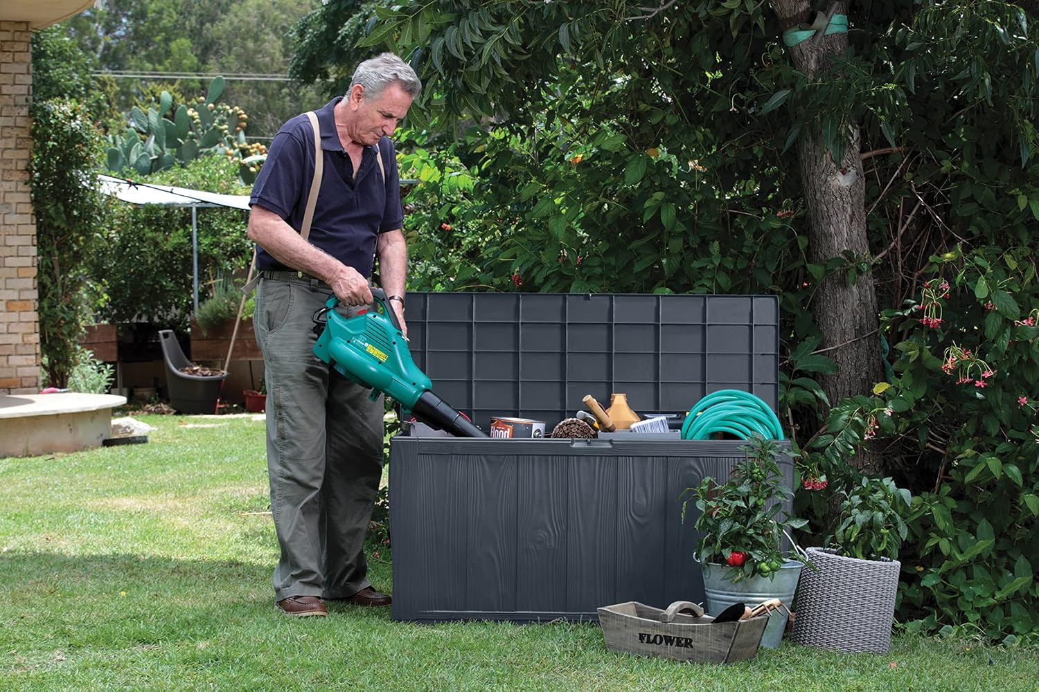 Man standing next to an open Keter Sherwood storage box, which contains garden tools