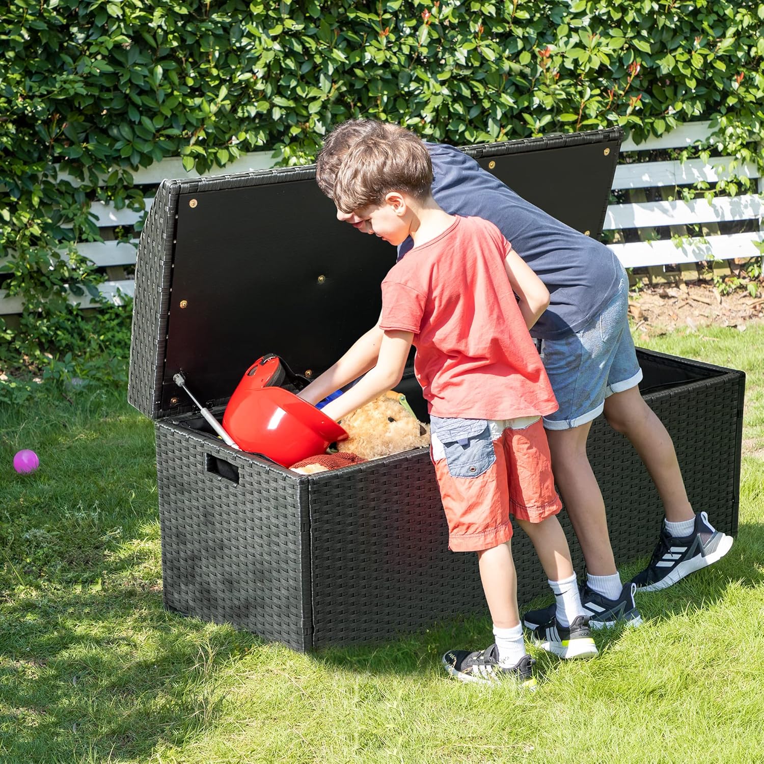 Two children placing toys into the open Devoko storage bench in a garden setting.