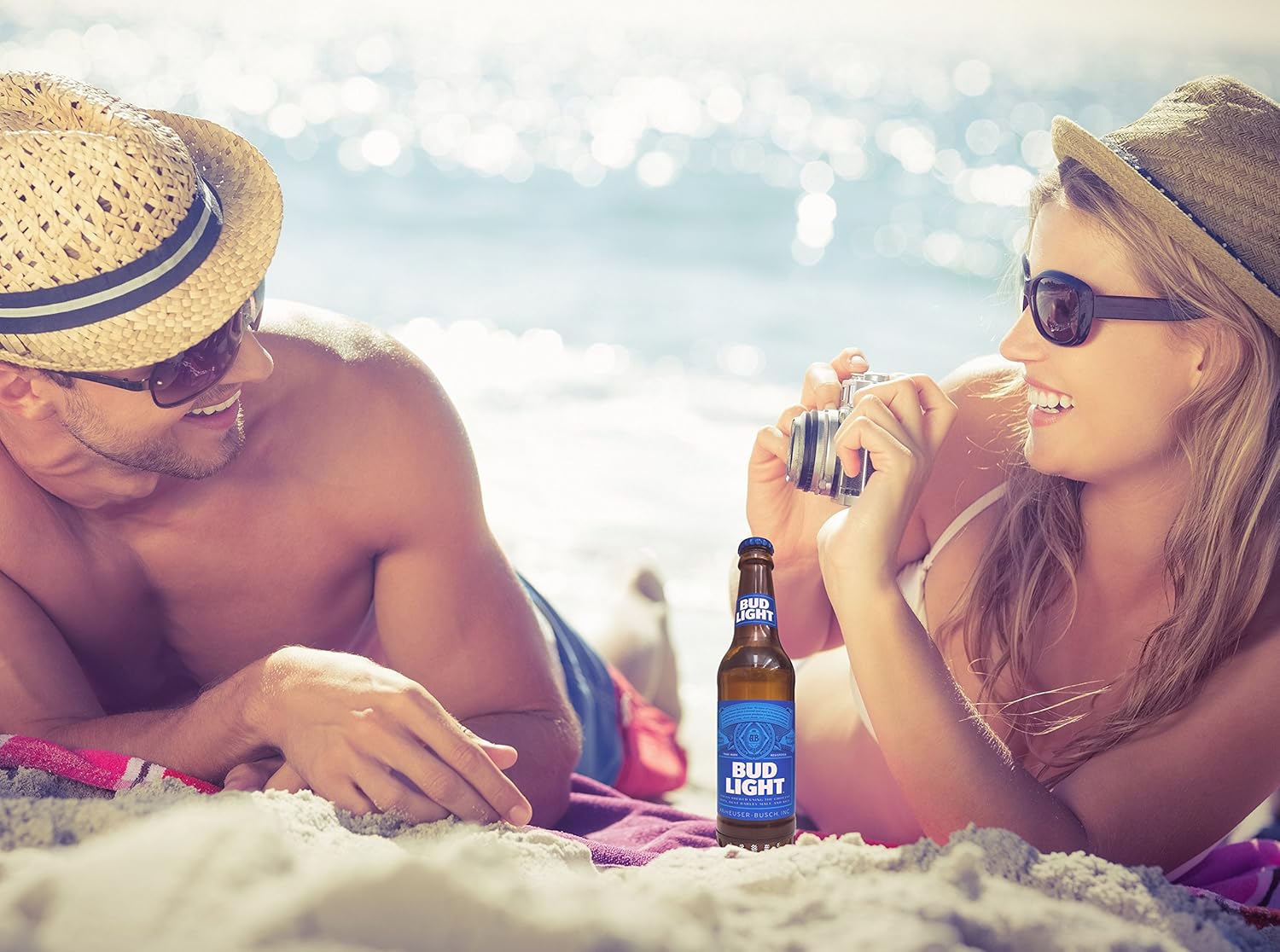 Couple relaxing on a beach with the Bud Light Bluetooth Speaker between them