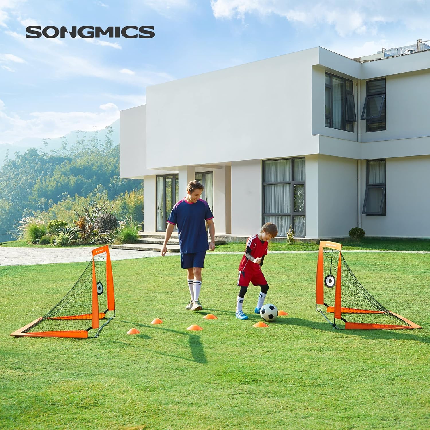 Two children playing soccer with the SONGMICS goals and training cones on a grassy lawn outside a modern house.