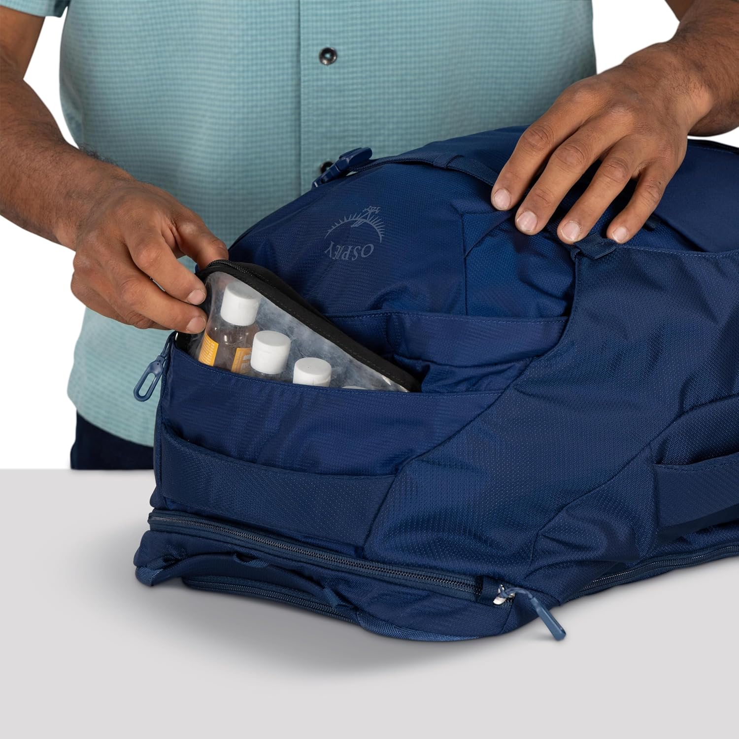 A hand opening the external zippered toiletry pocket of the Osprey Farpoint 40L backpack, revealing small bottles.