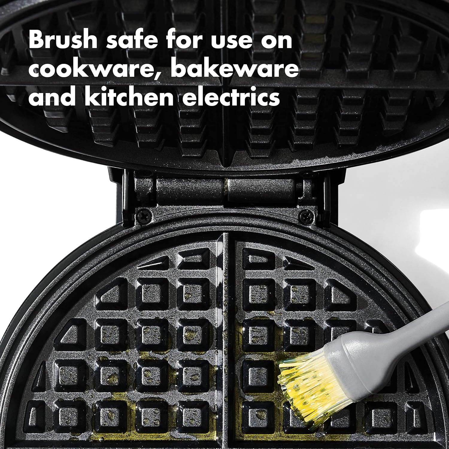 The OXO silicone brush applying oil to a waffle iron, showing its suitability for various cookware surfaces.