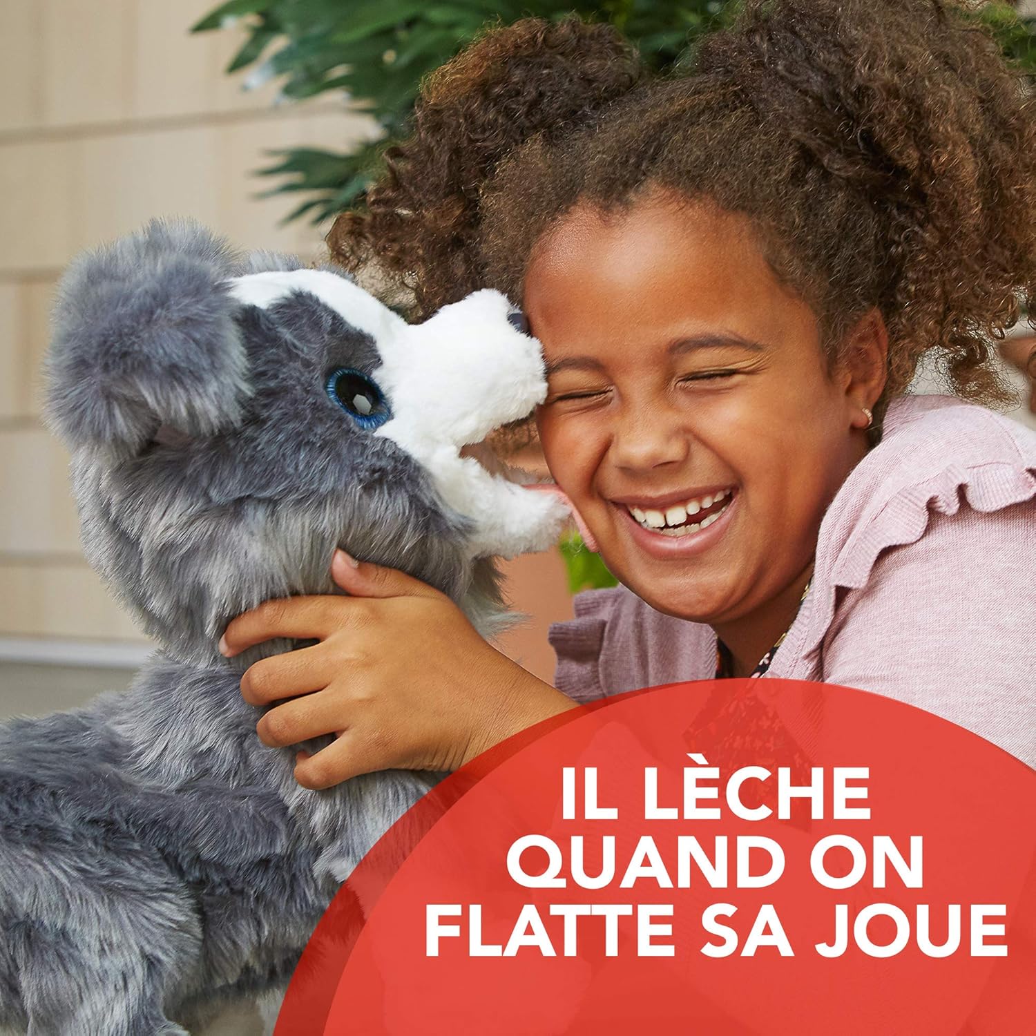 A child laughing as FurReal Friends Ricky My Little Dog licks their face, showing affection.