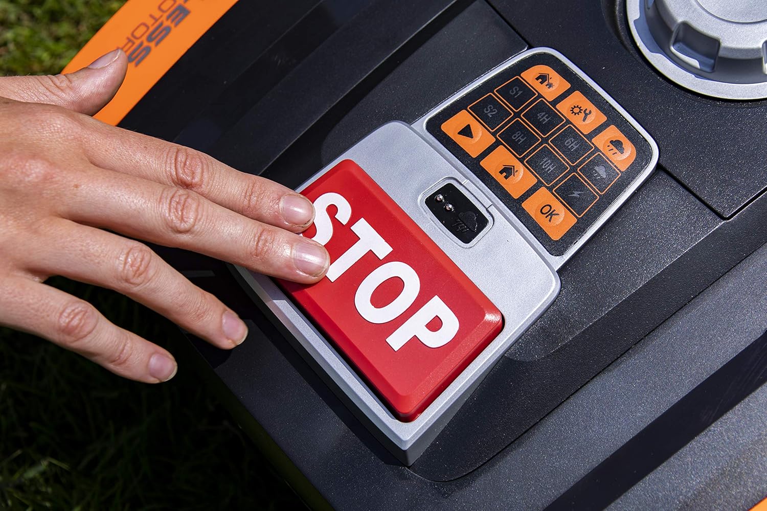 Hand pressing the large red STOP button on the mower's control panel