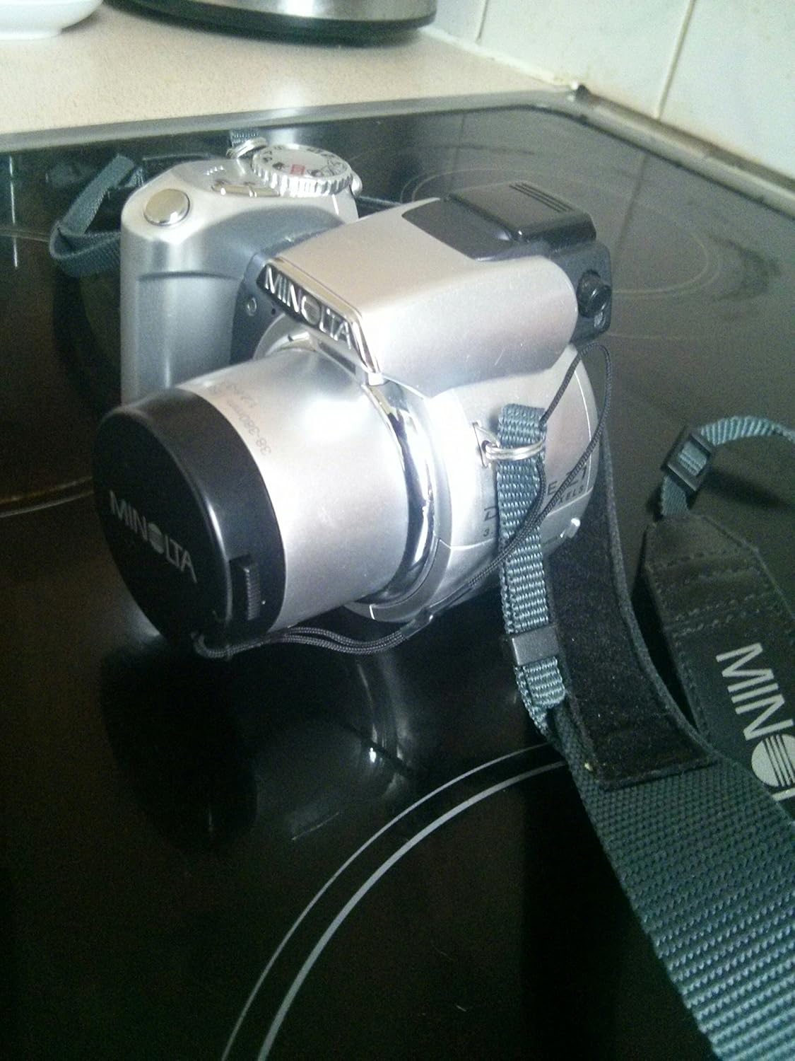 Frontal view de la càmera digital Minolta Dimage Z1 amb l'objectiu estès i la corretja per al coll fixada.