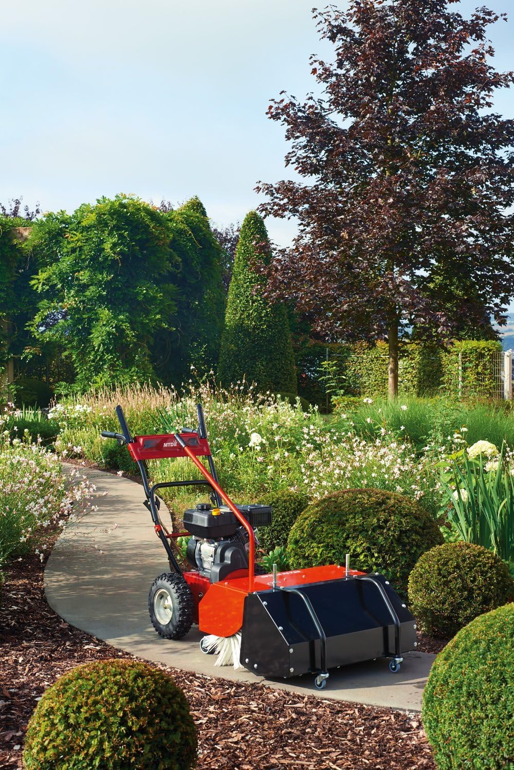 MTD Optima PS 700 sweeper with attached container in a garden setting.