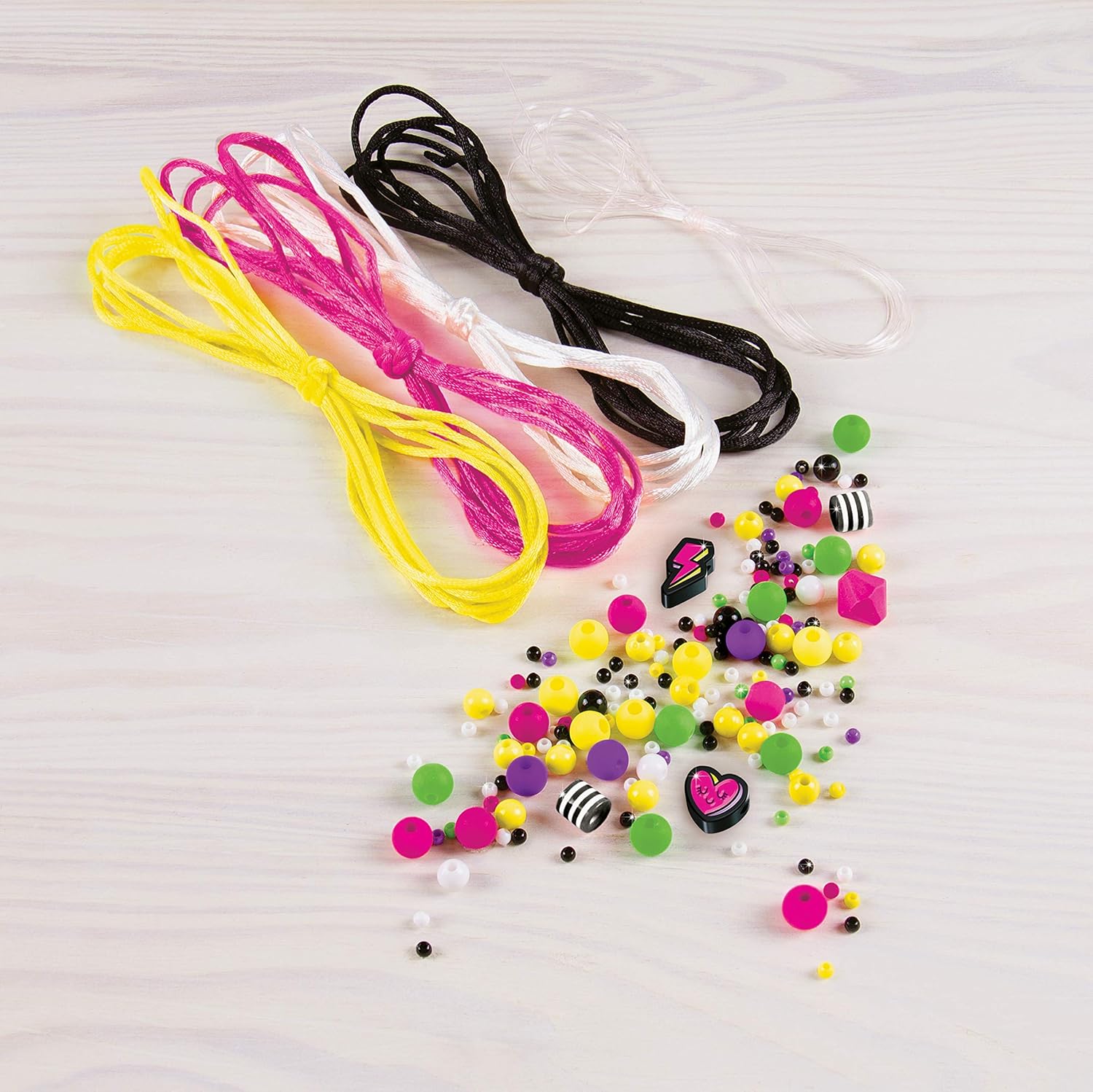 Contents of the Make It Real Neon Black & White Bracelets kit, showing various colored cords, a pile of assorted beads, and charms.