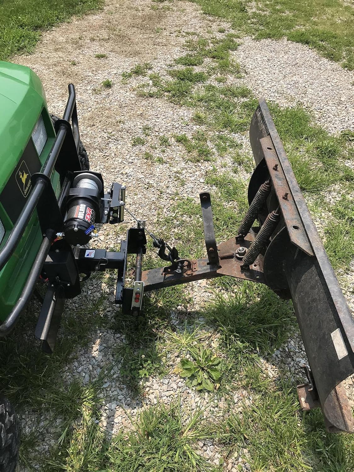 Green ATV with a snow plow attached, demonstrating the HFT Badland ZXR 2500 Lb. winch in action to raise the plow.