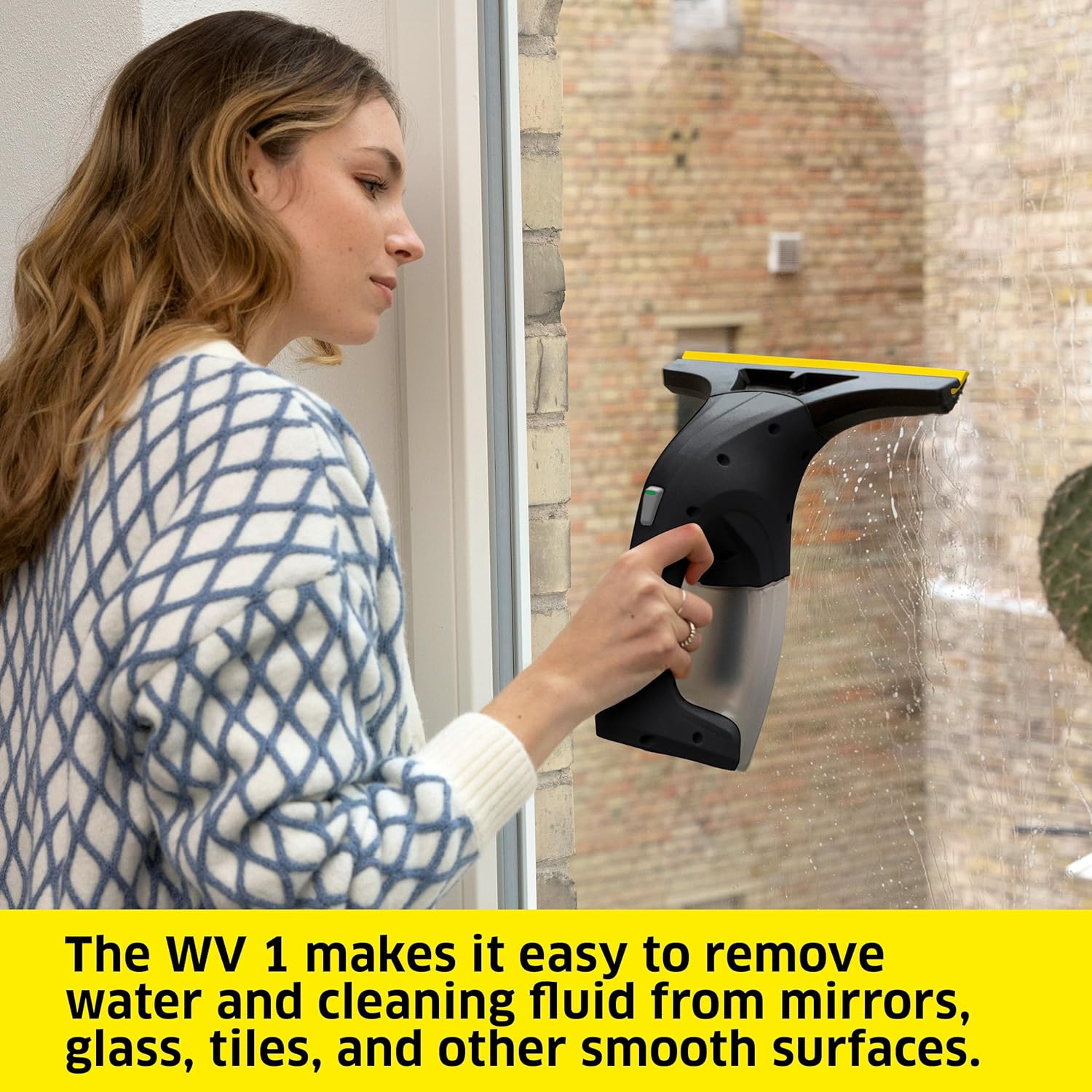 A woman using the Kärcher WV 1 Plus to clean a window, demonstrating the vacuuming action.