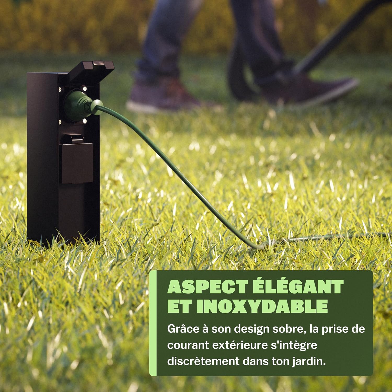 Monzana garden socket in a grassy area with a green power cable plugged into one of its sockets, demonstrating its use.