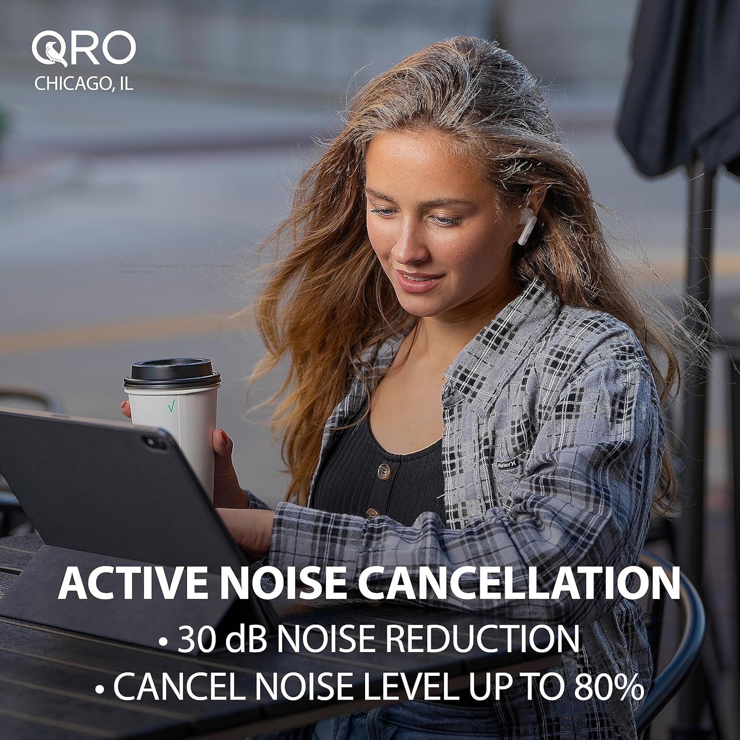 Woman wearing Qro earbuds, working on a laptop in a cafe, demonstrating Active Noise Cancellation