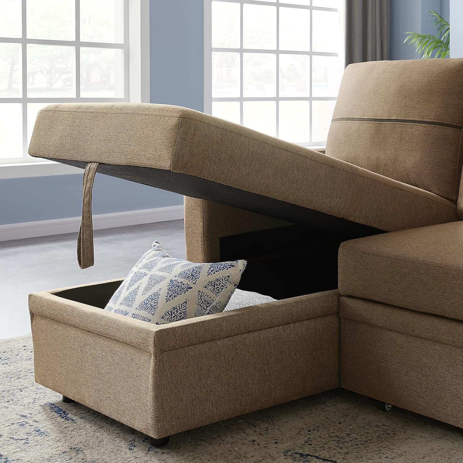 A close-up of the chaise section of the sofa with its top lifted, revealing a storage compartment containing a pillow.