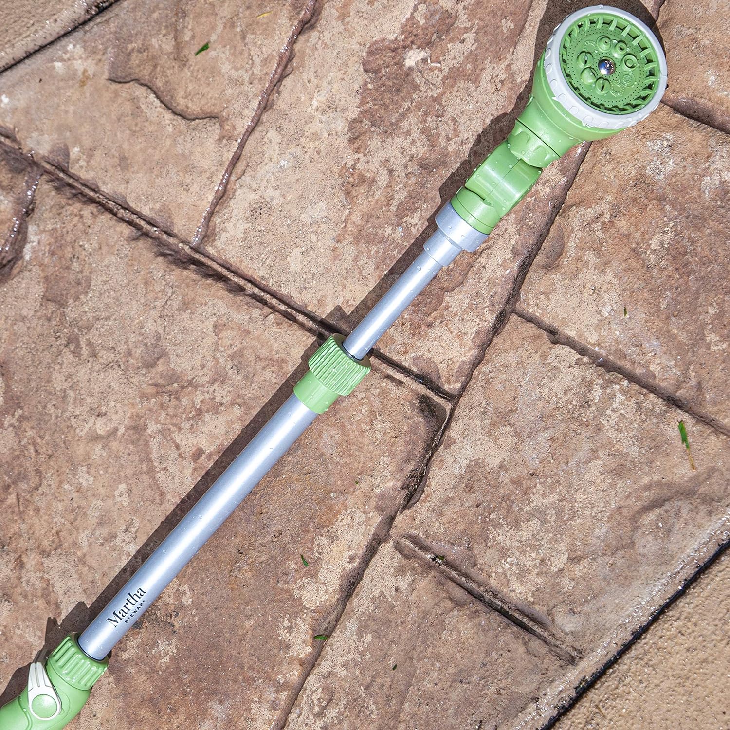 The Martha Stewart watering wand lying on a stone patio, showing its length and design in a natural setting.
