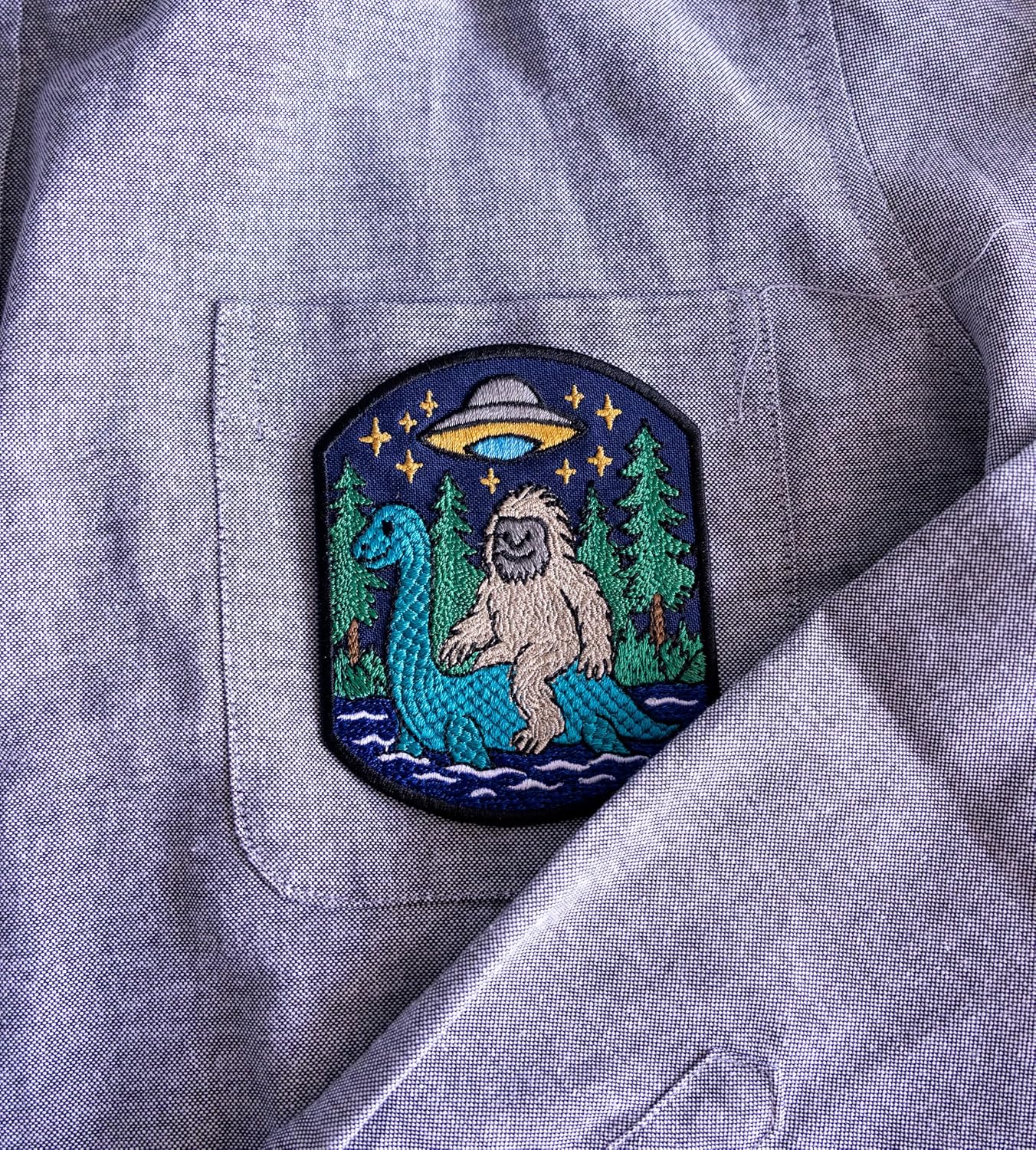 A Bigfoot Rides The Loch Ness Monster While a Flying Saucer Watches him in The Night Sky. Embroidered Patch Iron On. Size: 3.8x3.1 inches.