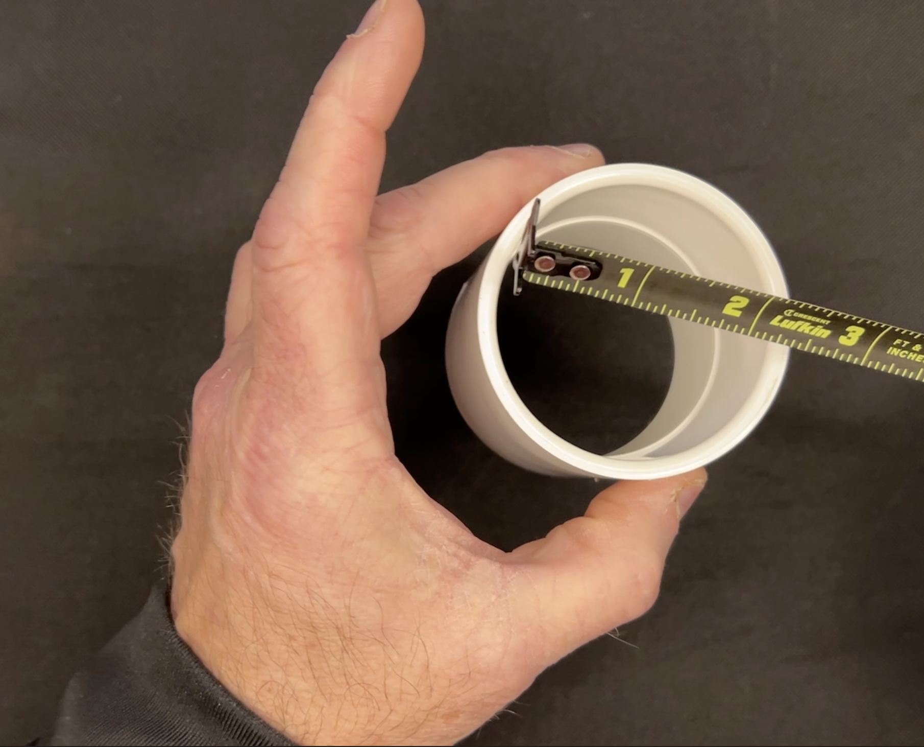 A hand holding a white PVC coupler, demonstrating its 2-inch internal diameter for plumbing connections.
