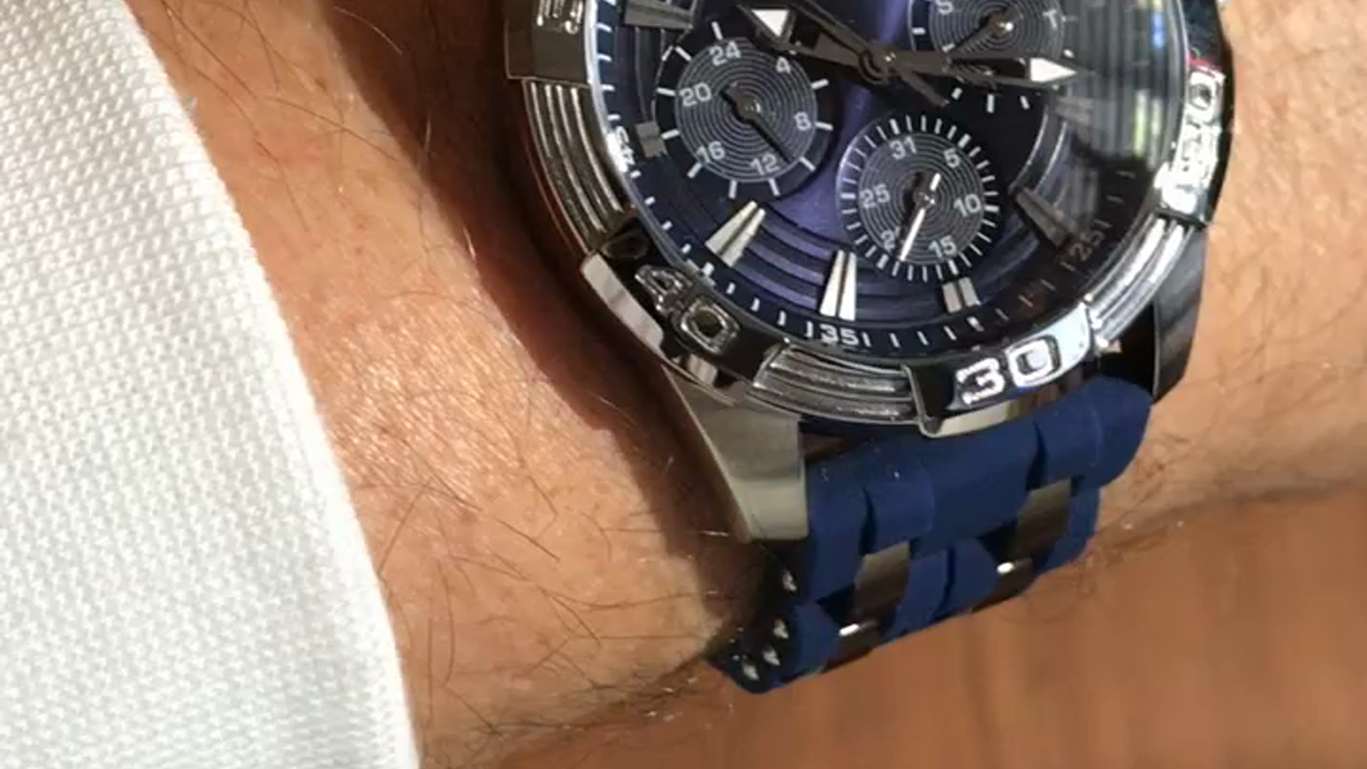 GUESS Iconic Blue watch on a wrist, showing the blue silicone band and silver-tone case.