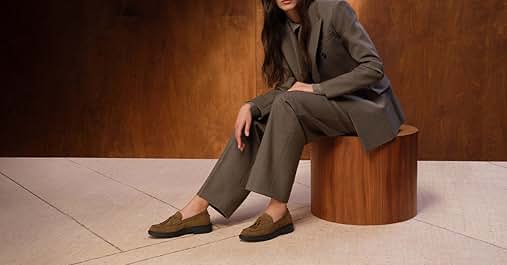 El texto dice «Imagen 1". Mitad inferior de una persona sentada en un asiento cilíndrico de madera, vestida con un traje gris y mocasines marrones. Visible sobre un fondo de tonos cálidos