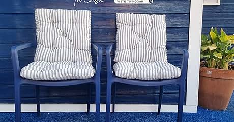 Dos sillas de exterior azules con cojines acolchados a rayas grises y blancas, colocadas contra una pared de madera azul marino