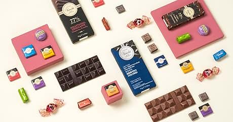 Surtido de barras de chocolate, caramelos y productos de confitería dispuestos sobre una superficie rosa. Se ven varias barras de chocolate, tanto negro como con leche, junto con caramelos y chocolates envueltos en colores