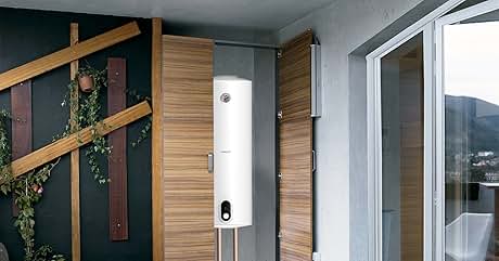 montado en la pared de un balcón moderno con puertas con paneles de madera, piso de concreto y puerta corredera de vidrio. Asientos al aire libre y plantas visibles.