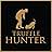 Gold logo on black background featuring silhouette of person bending towards small dog. Text below reads 'TRUFFLE HUNTER'.