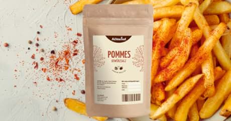 Der Text lautet „POMMES épicées“. Braune Papiertüte mit Produktetikett. Der Hintergrund zeigt verstreute Gewürze und goldene Pommes frites. Die Packung enthält wahrscheinlich Gewürze für Pommes oder Kartoffeln