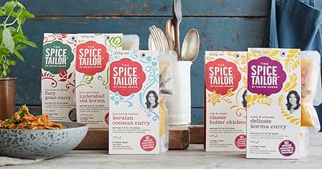 Display of plant-based protein powder packages from 'The Protein Works' brand, showcasing multiple flavors on a rustic wooden surface with kitchen accessories.
