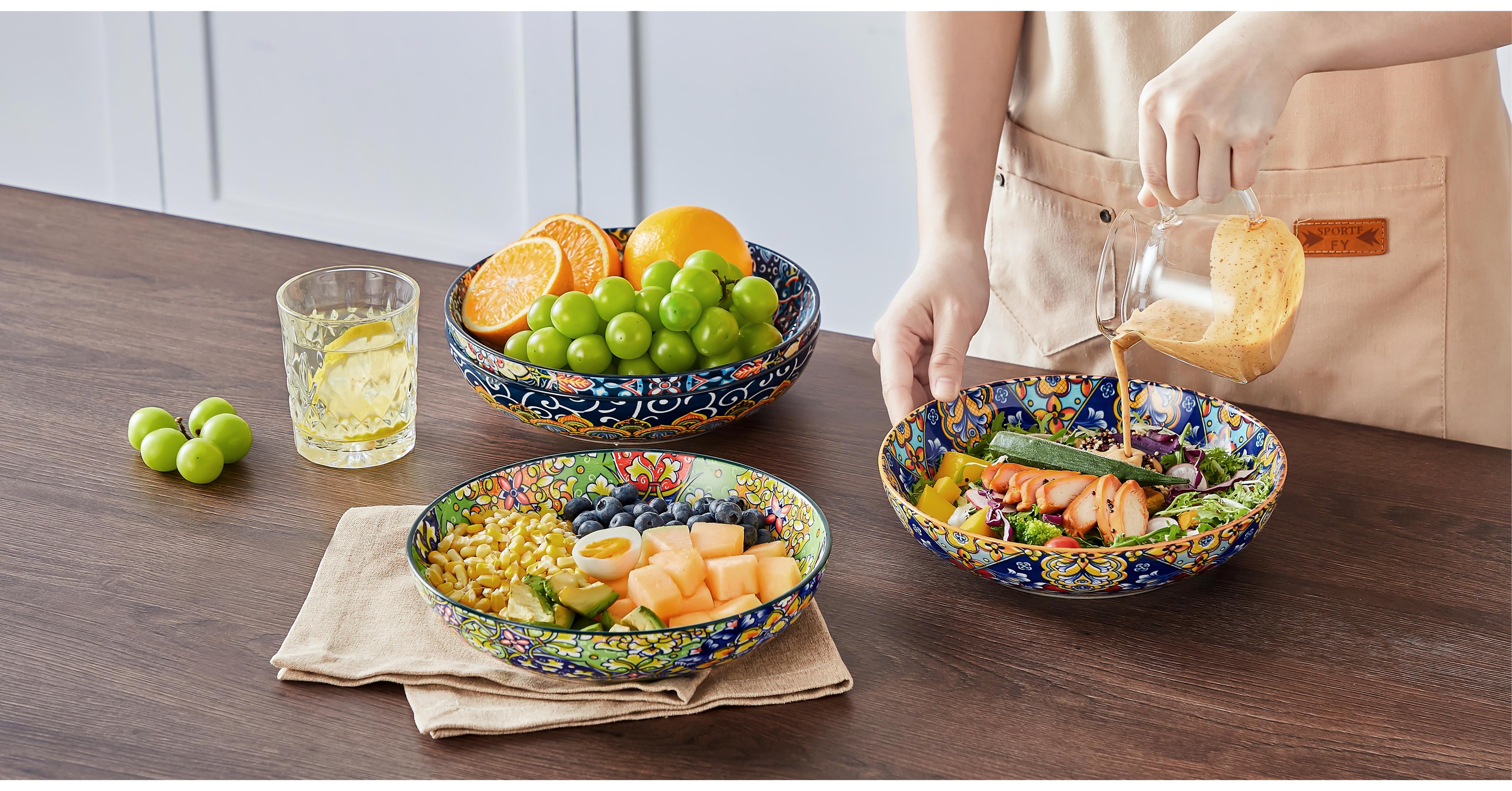 Colorful dining scene with bowls of citrus fruits and grapes, served meals, and hands pouring drinks on wooden table.