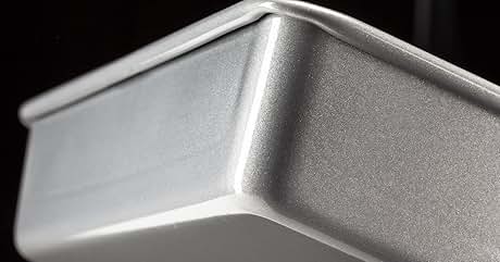 Close-up of a brushed aluminum or metal container with angular edges, showing textured matte surface finish under dramatic lighting.