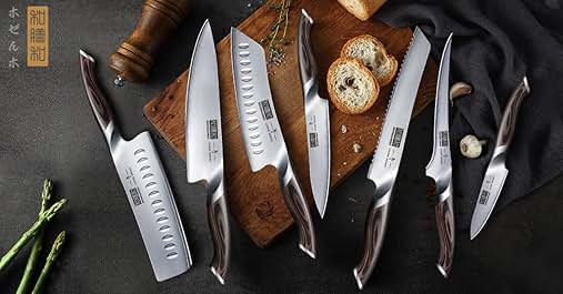 Professional knife set with hollow-ground blades displayed on dark surface with wooden cutting board, bread slices, and asparagus stalks visible.