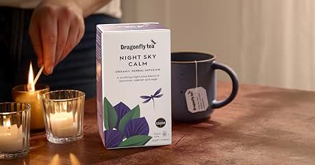 Box of 'Night Sky Calm' herbal tea by Republic of Tea, placed on table with lit candles and blue mug. Packaging features purple lotus and dragonfly design.
