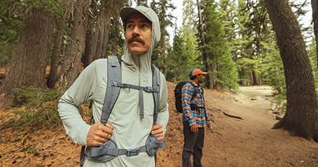Mochila de senderismo gris claro usada por una persona en un sendero forestal. Correas acolchadas para los hombros, correa para el pecho y cinturón visibles. Otro excursionista en segundo plano