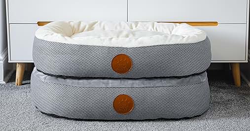 Two stacked circular pet beds with gray fabric covers and brown leather accents. White plush interior visible on top bed.