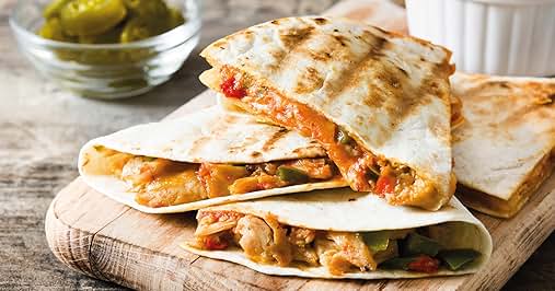 Grilled quesadillas on wooden board. Filled with orange-colored mixture, likely chicken. Cut into triangles, showing melted cheese and filling. Bowl of olives nearby.