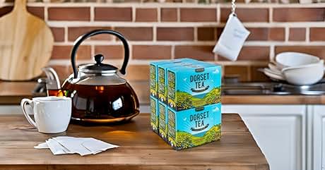 Kitchen counter with black kettle, white cup, and two stacks of green tea boxes. Brick wall background and partial view of kitchen appliances.