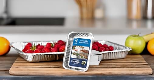 Disposable aluminum foil pans on wooden cutting board, with fresh strawberries visible in one pan. Citrus fruits visible in background.