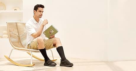 Persona con camisa blanca y pantalones cortos caqui sentada en una mecedora de madera, leyendo un libro. Llevaba calcetines y zapatos negros