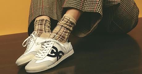 Text reads "SNEAKERS". White sneakers with black logo, worn with plaid pants and matching socks. Person sitting on wooden surface against orange background.