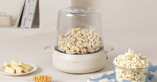compacta con cúpula de cristal rellena de palomitas. Base en blanco. Rodeado de palomitas de maíz, mantequilla y aperitivos sobre una superficie ligera
