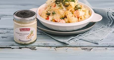 Creamy pasta dish in white bowl next to jar of horseradish sauce. Pasta appears to have a cheese-based sauce with green herbs sprinkled on top.