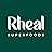 Logo for Rheal Superfoods, featuring white text on a dark green background. The brand name 'Rheal' is prominently displayed in a stylized font above 'SUPERFOODS' in smaller capital letters.