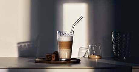 Bebida de café en capas en vaso alto con pajita, servida en un plato con un aperitivo en un ambiente de iluminación tenue