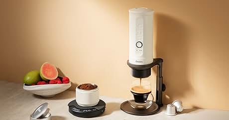 con diseño cilíndrico blanco, recipiente transparente y accesorios adjuntos en una superficie de madera junto a fruta fresca.