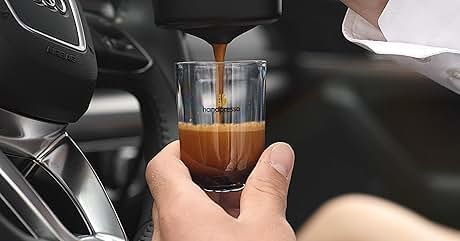 Un vaso de chupito de vidrio transparente que se llena con espresso o café de una máquina, muestra una formación de líquido oscuro y crema.