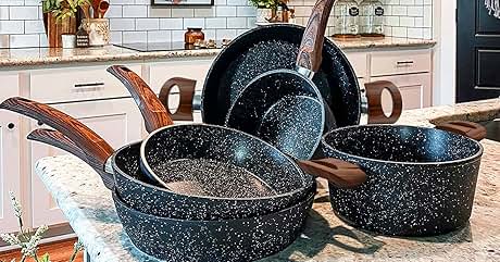 Set of black speckled cookware with wooden handles, including pots and pans, displayed on a kitchen counter with white cabinets and subway tile backsplash.