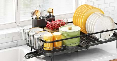 Expandable black dish drying rack with multiple compartments, holding plates, cups, and utensils on a white countertop beside kitchen items.